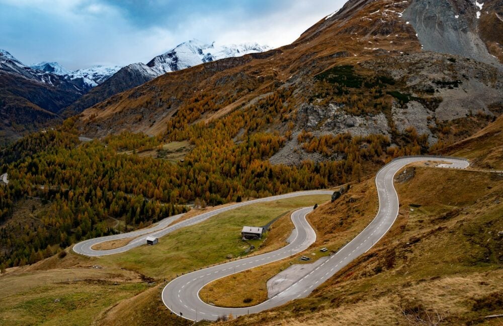 Winding Alpine pass road through autumn-coloured slopes below snowy peaks