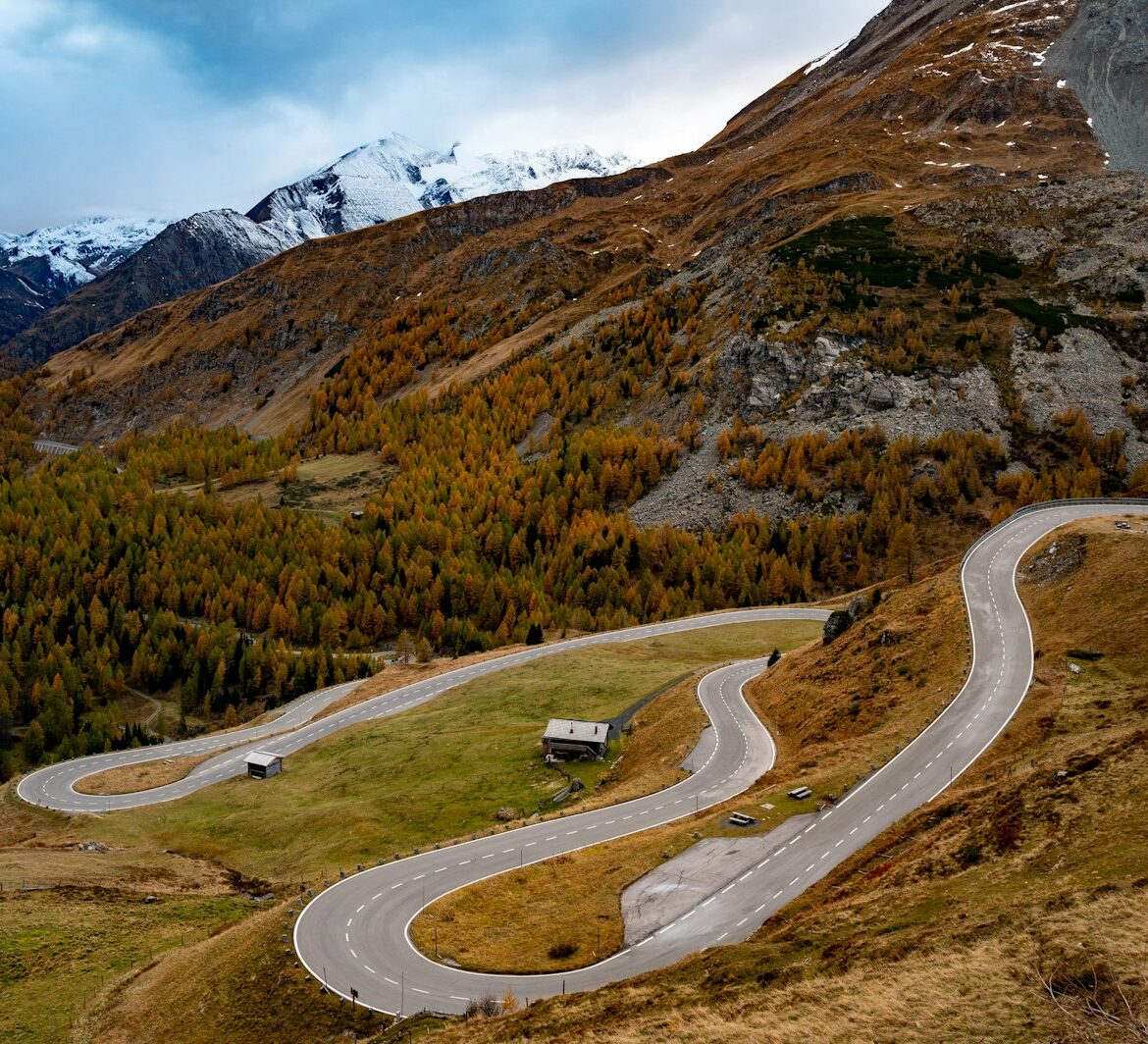 Winding Alpine pass road through autumn-coloured slopes below snowy peaks Winding Alpine pass road through autumn-coloured slopes below snowy peaks