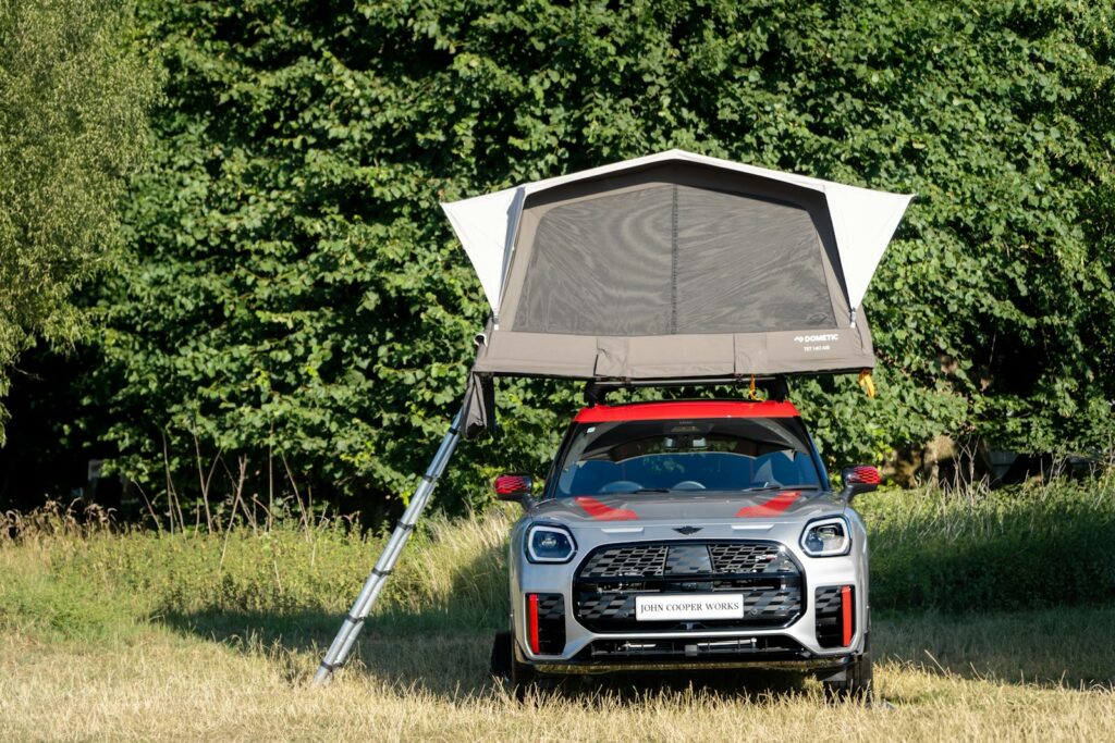 Small car with an opened rooftop tent and ladder parked on grass