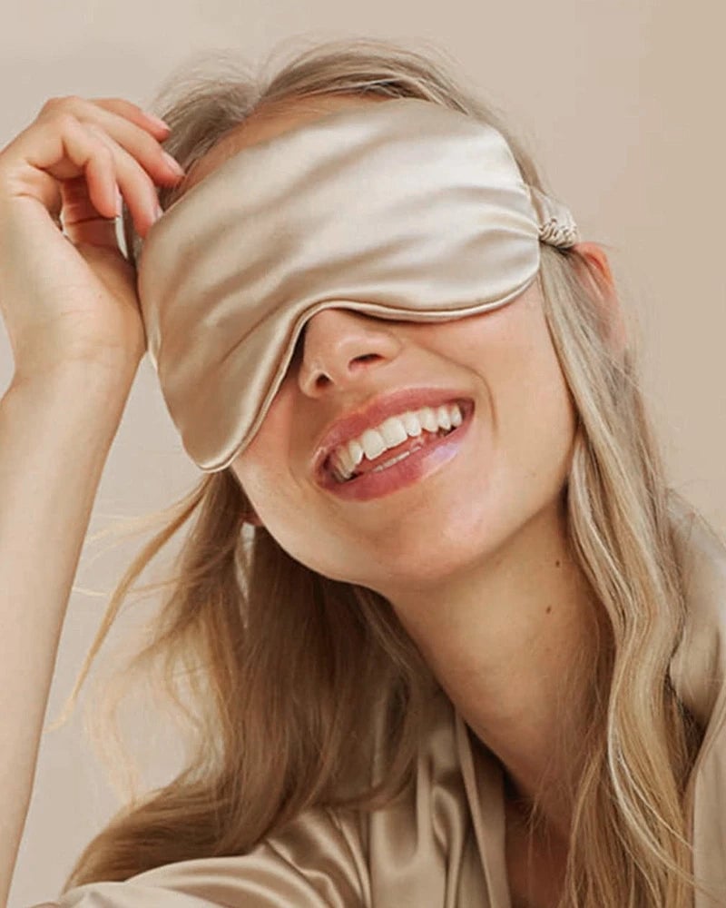 Woman lifting a champagne-coloured DAISYSILK 22 momme silk eye mask