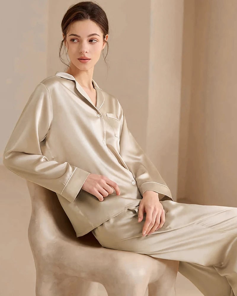 Woman in champagne washable silk pyjamas with contrast piping, seated