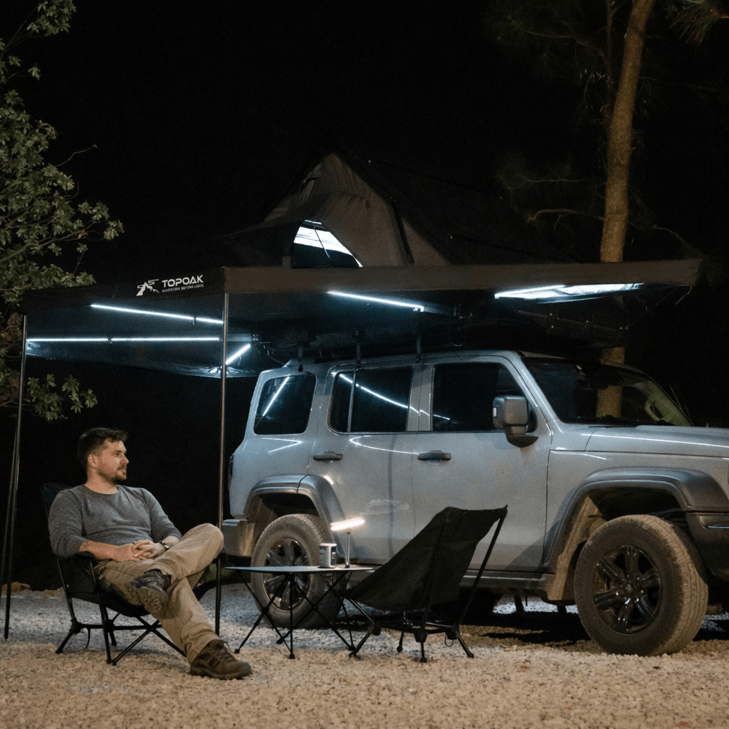 TOPOAK 270-degree awning lit at night beside an SUV with a rooftop tent and camping chairs
